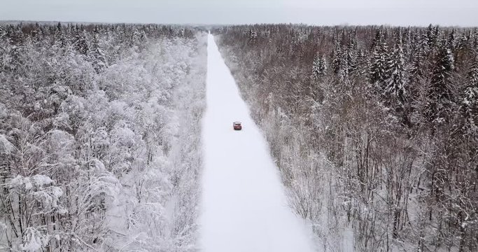 Aerial view of a snowy forest and road with orange car in the winter.