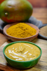 Tasty mango-curry sauce in small bowl ready to eat and bowls with mango and curry powder close up