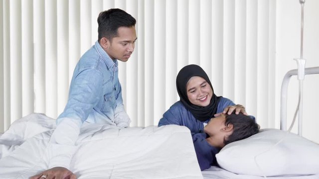 Two young parents talking with their sick son lying on bed in hospital room. Shot in 4k resolution