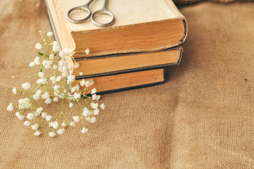 Vintage spring background with white flowers, a yellowed old books and the scissors on the burlap. closeup.