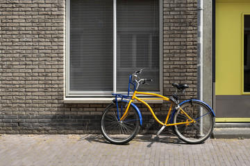 Fototapeta na wymiar The yellow bike is parked against the wall of a brick building.