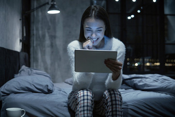 Photo of young woman sitting on bed with tablet communicating via video chat