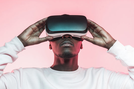 Fototapeta Portrait of African guy isolated on pink background wearing headset of virtual reality