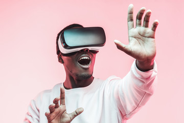 Young african man playing VR video game with virtual reality goggles and mouth wide open, trying to...