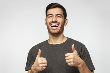 Motivated excited smiling young man making thumbs up gesture of approval and success