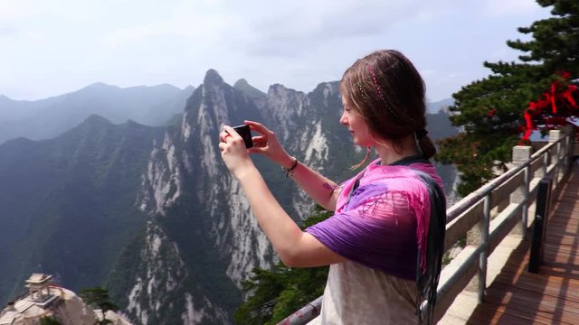 A hiker young woman admires the view of the mountains and takes a photo. The Chinese mountain Hua (Huashan) is one of the five great mountains of China, sacred place of Taoism. (Steadicam)