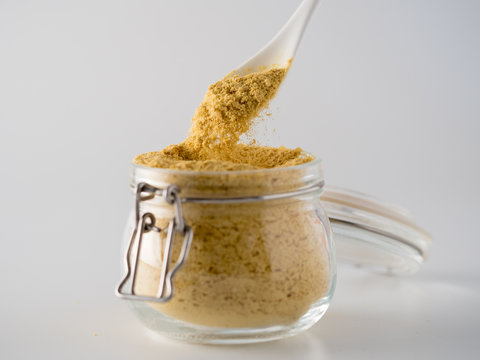 Nutritional yeast background. Nutritional inactive yeast falling from spoon in glass jar on white background. Copy space. Nutritional yeast is vegetarian superfood with cheese flavor, for healthy diet