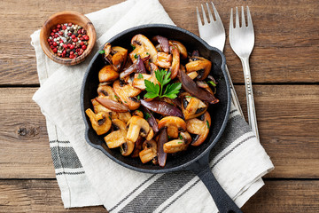 Fried mushrooms with fresh herbs in black cast iron pan.