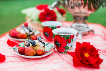 Samovar with a cup of morning tea, cinnamon buns and strawberry on the table on nature background