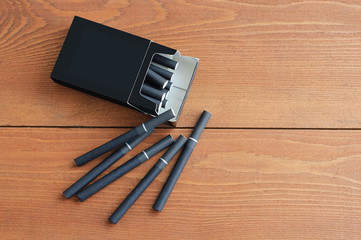 A pack of black cigarettes. Brown wooden background. Close-up.