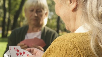 Smiling senior woman playing cards with friend outside, retirement free time