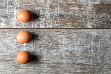 Three eggs in a vertical row with shadows on wooden background