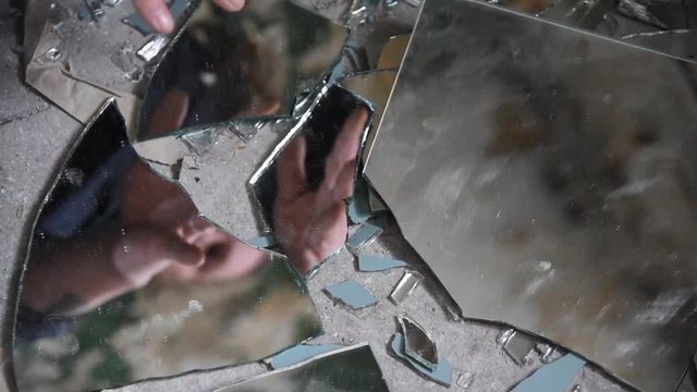 Depressed and angry man looks in shards of glass and reaches out for it