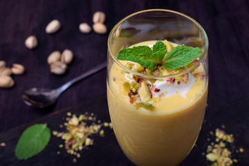 Mango yogurt dessert in a champagne glass topped with pistachios and mint against the dark background - obrazy, fototapety, plakaty