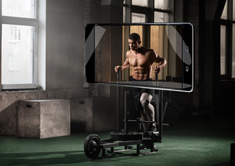 Fototapeta na wymiar Portrait of strong muscular man exercising in gym, smart device concept