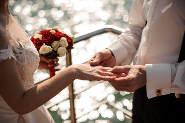 Broom putting on a golden wedding ring to a tender bride finger in background of the sea