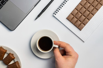 Snacking at work, have a bite concept. Laptop, candy and workbook with bar of chocolate. Men hand...