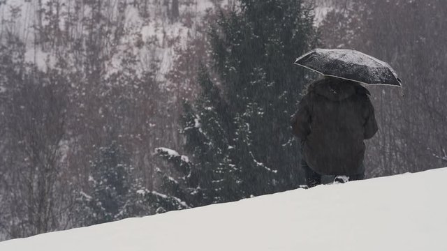 Man squatting in snow with umbrella and watching snow falling on the forest - (4K)