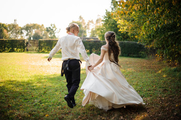 Back view of happy married couple running and laughing across the park