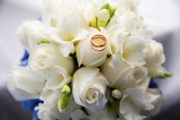 A pair of wedding rings on a bouquet of white roses, close up shot
