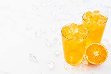 Fresh orange juice in tall glass with orange and ice on white marble table. Copy space for text....