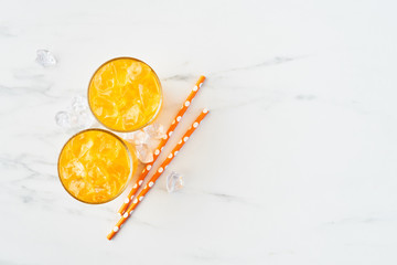 Fresh orange, mango or lemon juice in tall glass with ice and straws on white marble background. Summer drink. Top view. Copy space for text.
