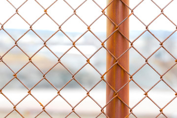 A closeup of a section of a rusty chain link fence. One fence post is visible. Industrial site in...