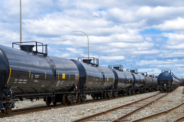 Fototapeta na wymiar Black railway tanker cars of the type used to transport petroleum products. Several cars visible on two separate sets of tracks. Identification markings have been removed, only technical info remains.