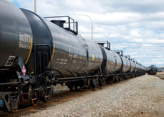Black railway tanker cars of the type used to transport petroleum products. Several cars visible on...