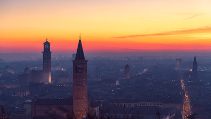 Beautiful panoramic sunset view of old town of Verona, Torre Lamberti and Santa Anastasia bell tower covered with evening fog. View from Piazzale Castel S. Pietro. Winter time. Verona, Italy