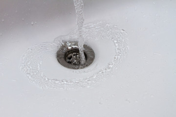 Water running into sink drain closeup. Drop of water falling in slow motion