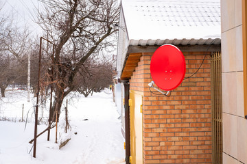 antenna for receiving satellite TV red attached to the brick wall of the house