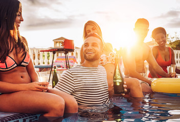 Group of happy friends making a pool party drinking champagne at sunset on vacation - Young people...