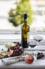 Cheese platter and glasses with wine on a window sill