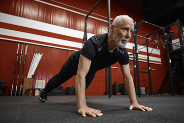 Handsome self determined Caucasian elderly man with white beard doing push ups to strengthen core...