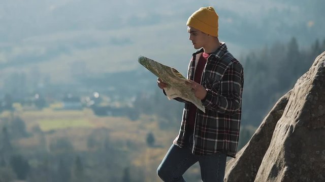 Travelling to the mountains. Hiker man holds old map standing on the top of the rock. The tourist travels in beautiful mountains