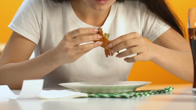 Hungry woman eating burger with appetite, fast food addict gaining excess weight