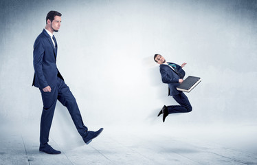 Big businessman kicking small businessman who is flying away with his briefcase on his hand
