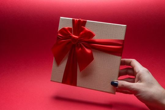 white gift box with a red bow in his hand on a red background.