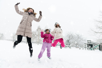 Happy mother and daughters jumping in a wintry park