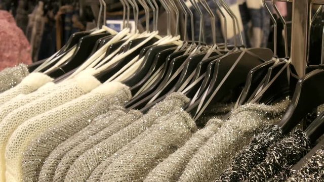 Row of beautiful warm women's fluffy sweaters of gray, black and white are hanging on black hangers in the store of the shopping center or mall. Fashionable collection of warm clothes.