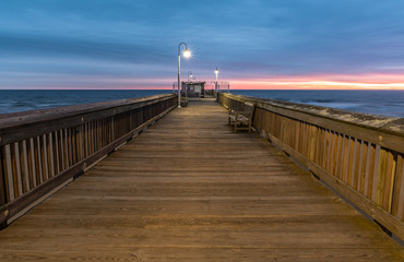 Sunrise from the Sandbridge Fishing Pier on Little Island Park in Virginia Beach.  The wood of the pier is lit by early morning sun rising in the clouds, creating pink and purple light.