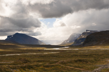 Fototapeta premium Valley with mountains in the distance and water flowing through a river during the hike of Kungsleden (Kings path) in northern Sweden.