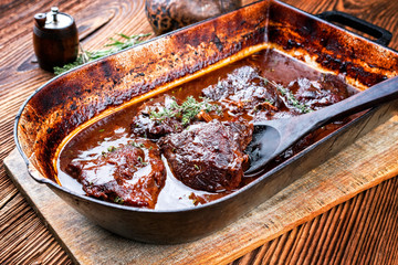 Traditionelle geschmorte Kalbsbäckchen in brauner Rotwein Sauce mit Pilzen und Zwiebel als closeup in einem Schmortopf