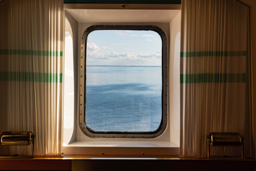 A view from the porthole window of a cruise ship, showing the sea and sunset