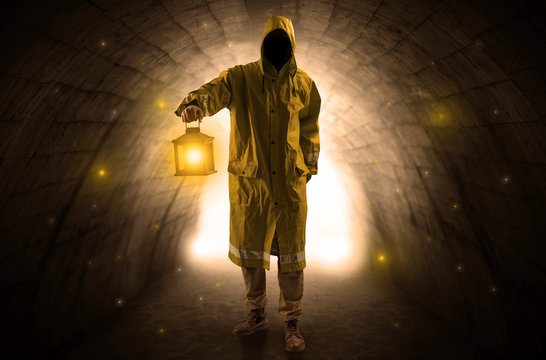Ugly man in raincoat walking with glowing lantern in a dark tunnel