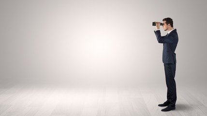 Businessman looking forward with binoculars in an empty space
