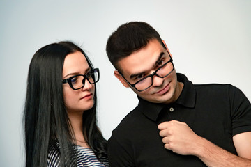 Serious loving brunette woman in eyeglasses examines her boyfriend looking at camera. Tender girl in eyeglasses looking with love at her man and he is looking out of his trendy glasses.