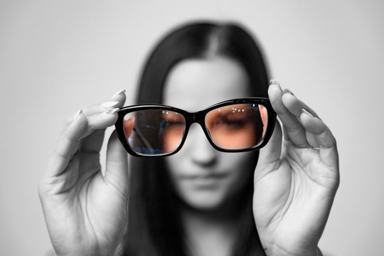 Beautiful Girl Is Holding Colorful Eyeglasses Right In Front Of Camera With Two Hands. Black And White Photo Of Woman With Color Glasses