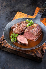 Traditional barbecue aged saddle of venison with herbs game sauce as closeup in a wrought iron skillet with copy space